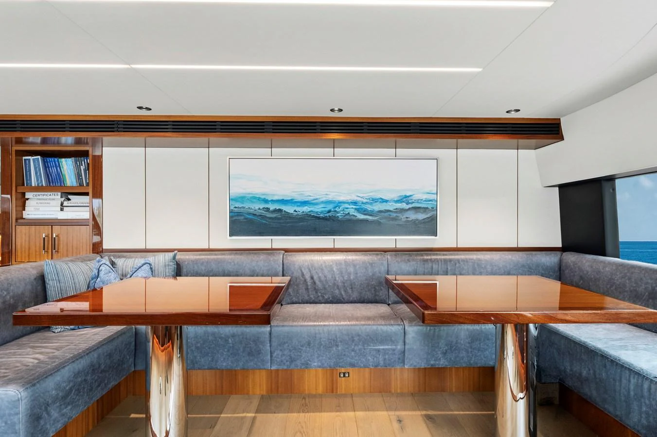 The salon features plush seating, polished wooden tables, and a large ocean-themed painting, creating a serene and elegant atmosphere. aboard SEAS THE DAY Yacht for Sale