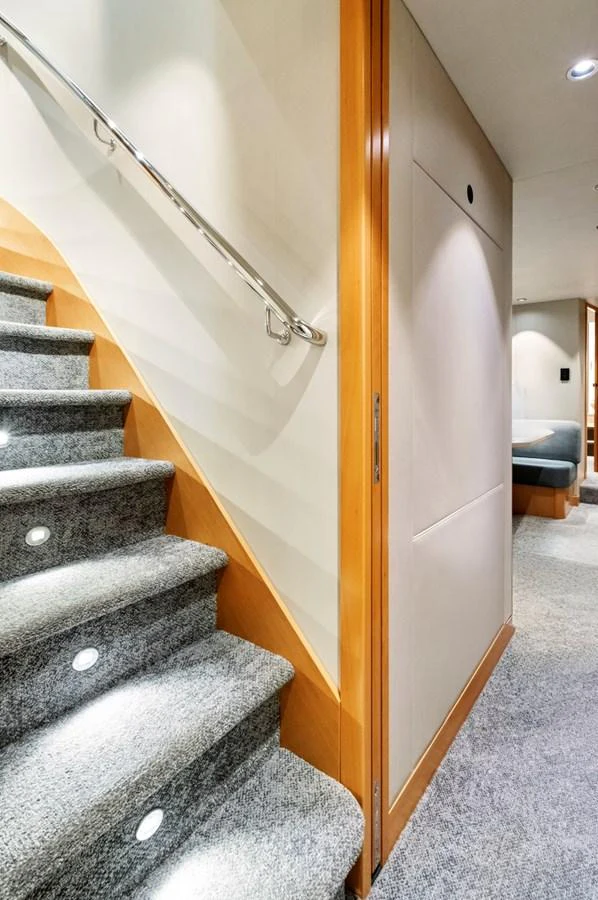 A well-lit interior staircase with modern design elements and plush carpeting. aboard SEAS THE DAY Yacht for Sale