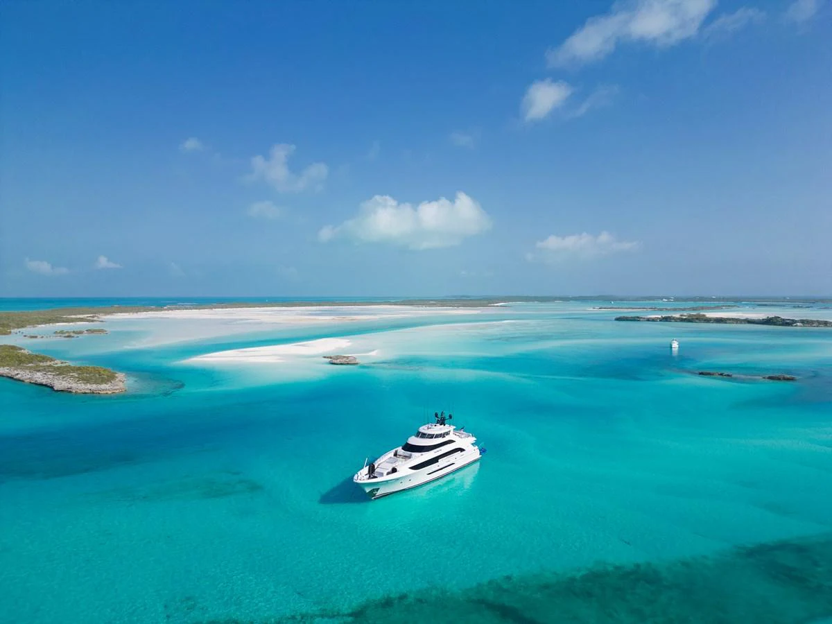 A luxurious yacht cruises through pristine turquoise waters against a backdrop of a serene sandy island. aboard SEAS THE DAY Yacht for Sale