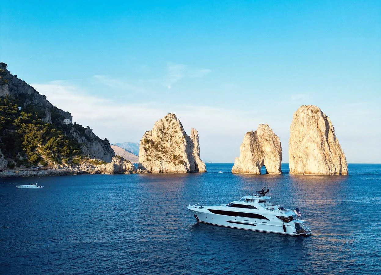 A sleek yacht cruises through serene blue waters with stunning rock formations in the background. aboard SEAS THE DAY Yacht for Sale