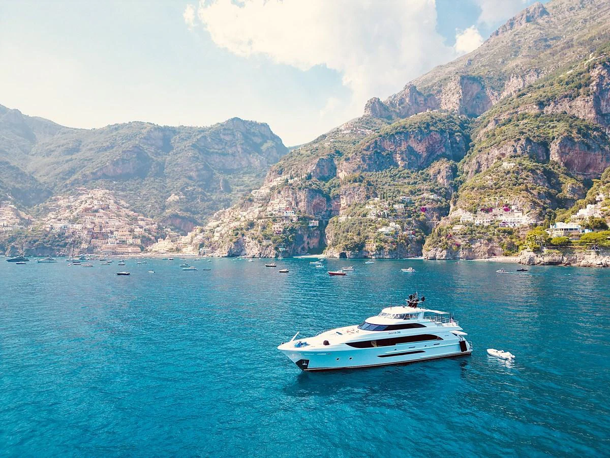 A sleek yacht cruises along a stunning coastal landscape with mountainous terrain in the background. aboard SEAS THE DAY Yacht for Sale