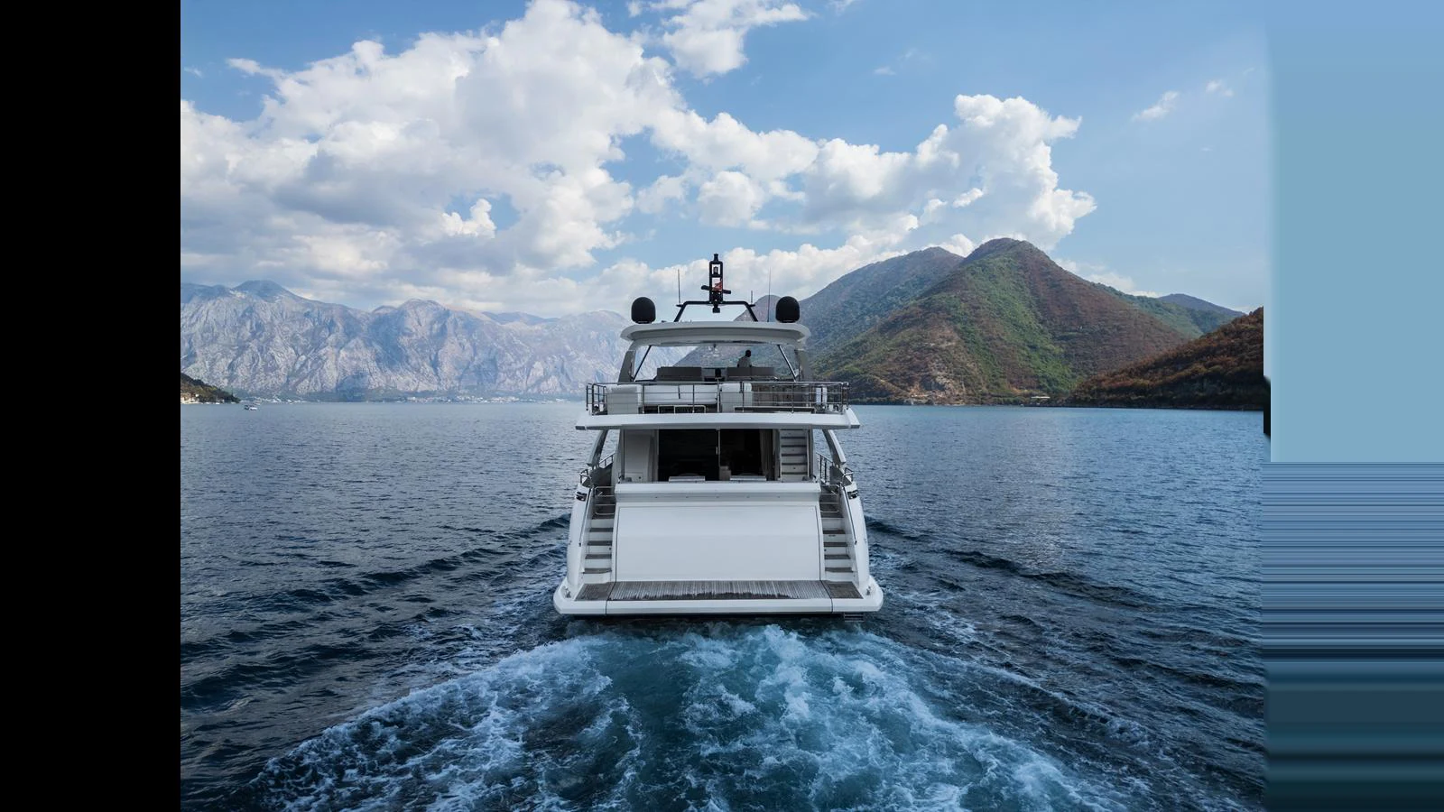 A luxurious yacht cruises through serene waters with a stunning mountain backdrop. aboard 98.92' AZIMUT GRANDE Yacht for Sale