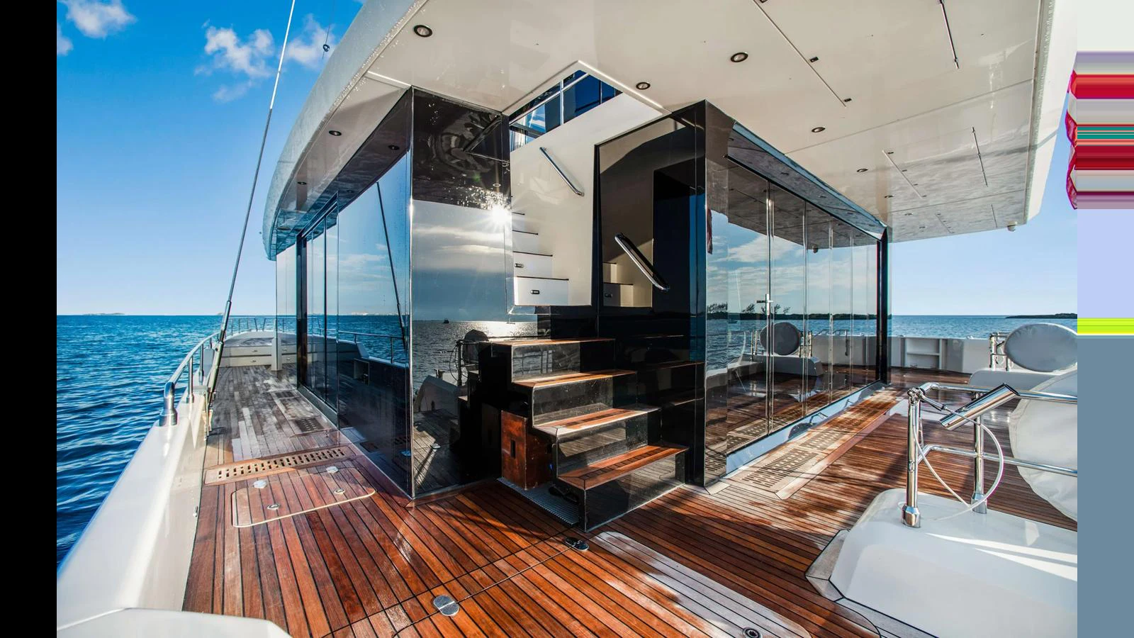 The aft deck features sleek glass doors, polished wood flooring, and a staircase leading to the upper deck. aboard MIDORI Yacht for Sale