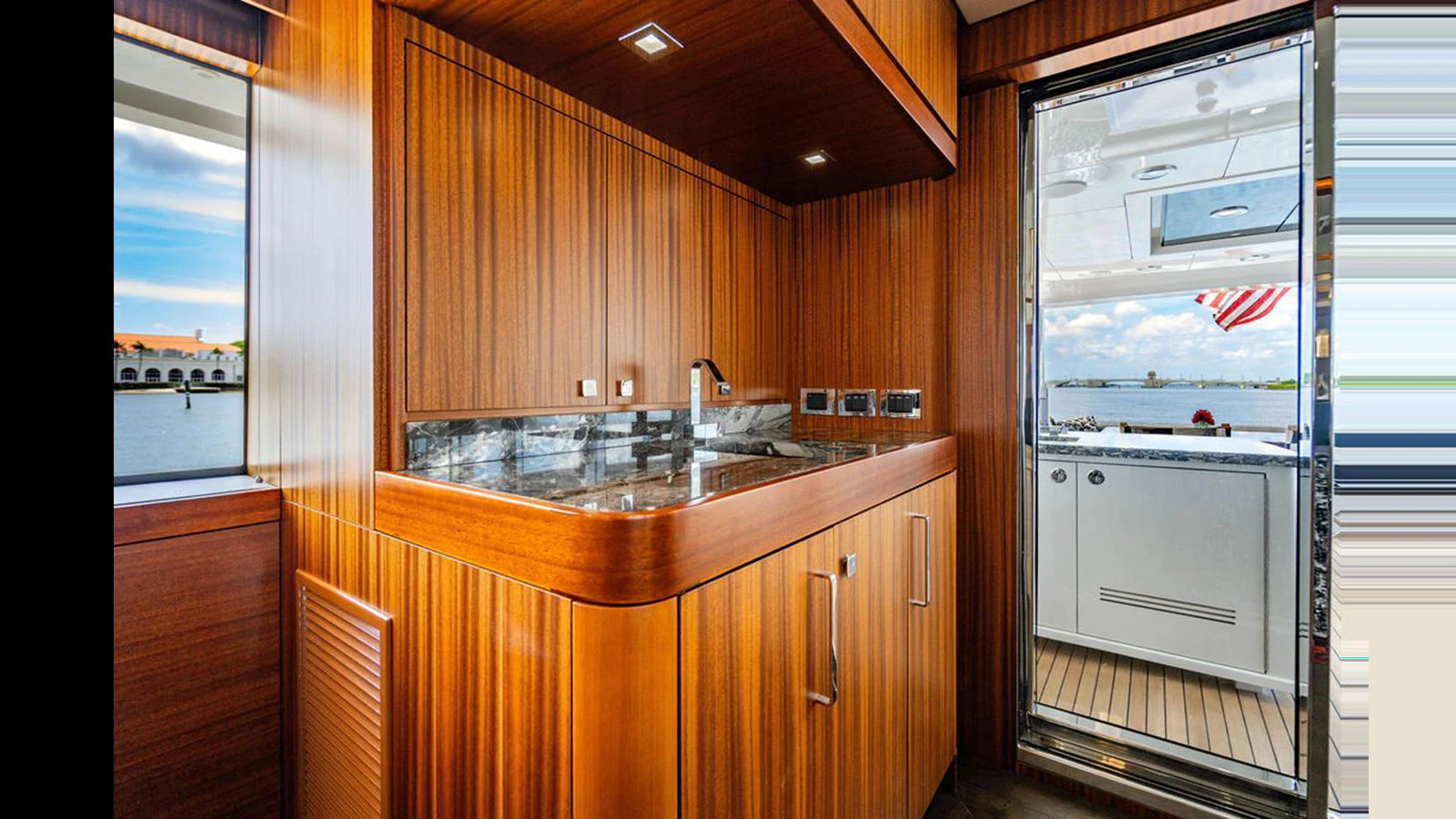 The yacht's galley features rich wood cabinetry and modern appliances, with a view leading to the exterior deck. aboard TRU LUV Yacht for Sale