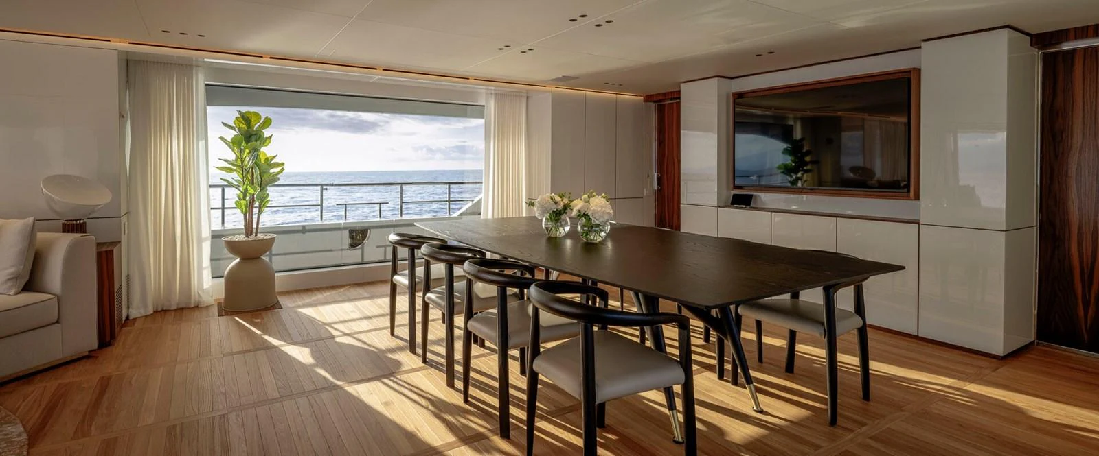 The yacht's dining area features a sleek table with modern chairs, complemented by a large window offering a stunning sea view. aboard CADA DIA Yacht for Sale