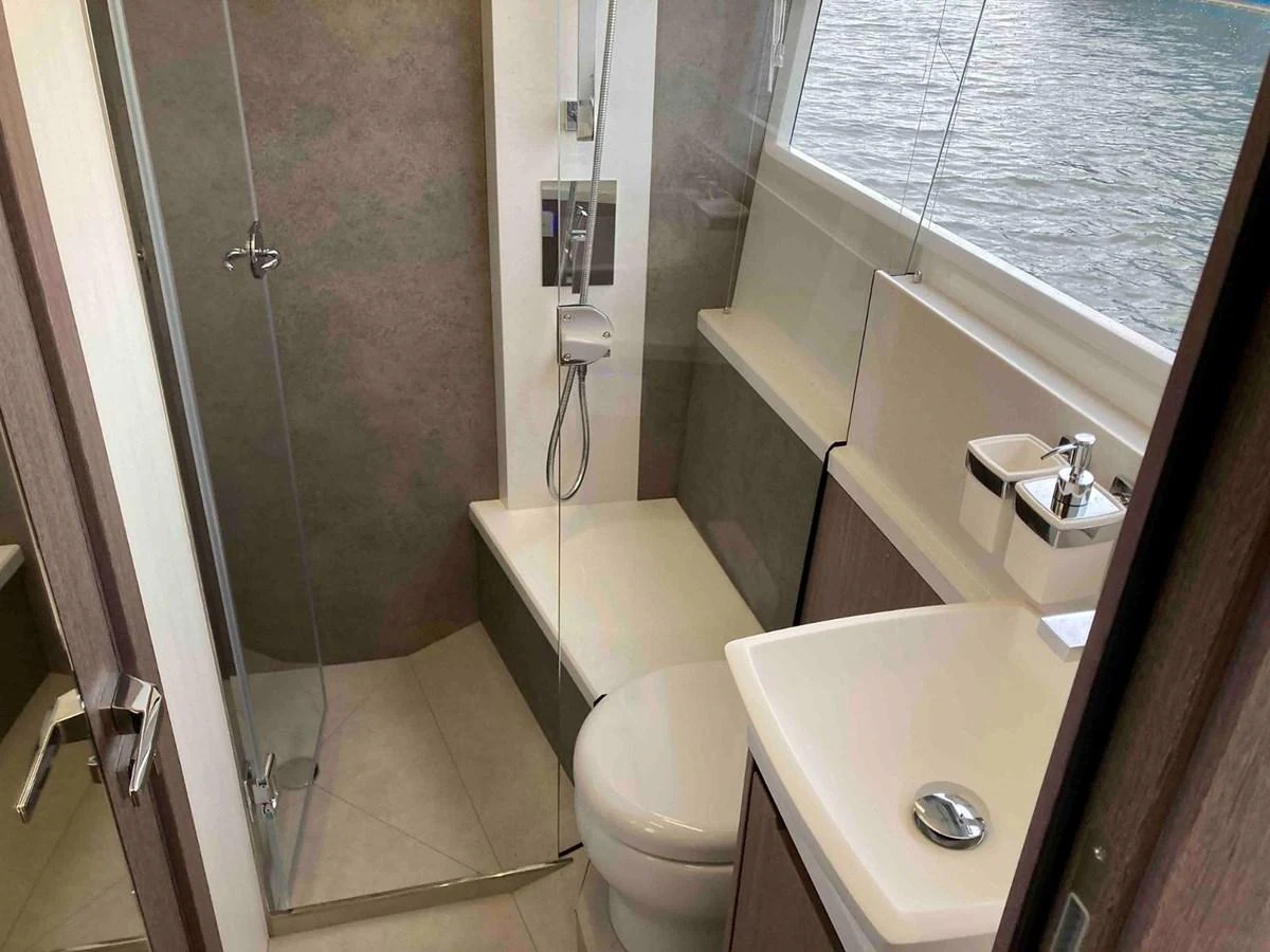 A compact and modern yacht bathroom with a shower, toilet, and sink, featuring a window with a view of the water. aboard GLN Yacht for Sale