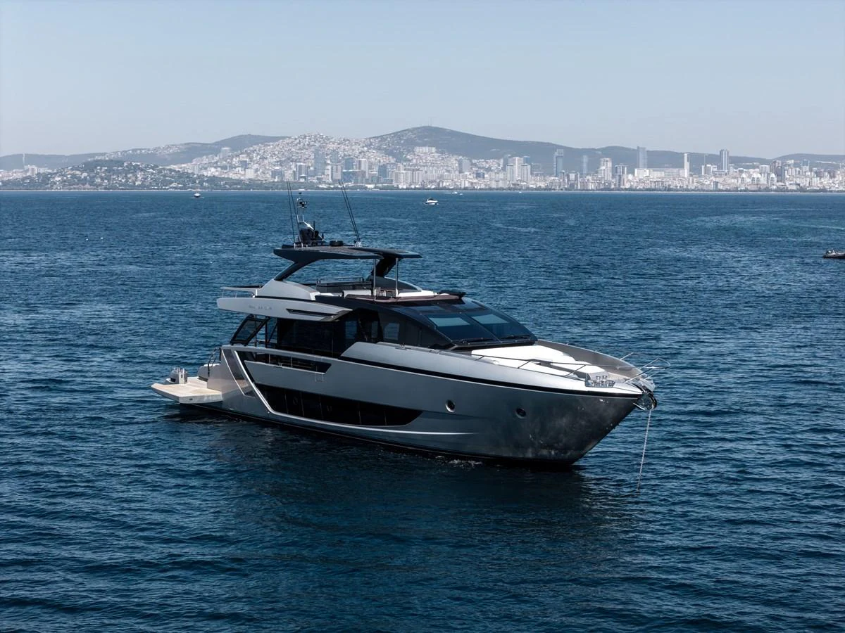 A sleek and modern yacht cruising on calm waters with a cityscape in the background. aboard CREA Yacht for Sale