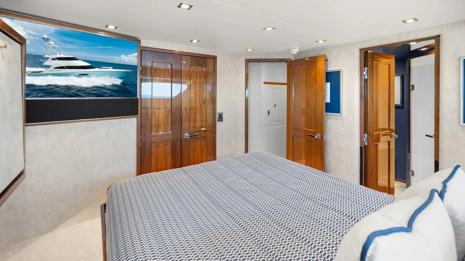 A luxurious stateroom featuring a large bed, wooden doors, and a wall-mounted TV displaying a yacht. aboard DOUBLE BARREL Yacht for Sale