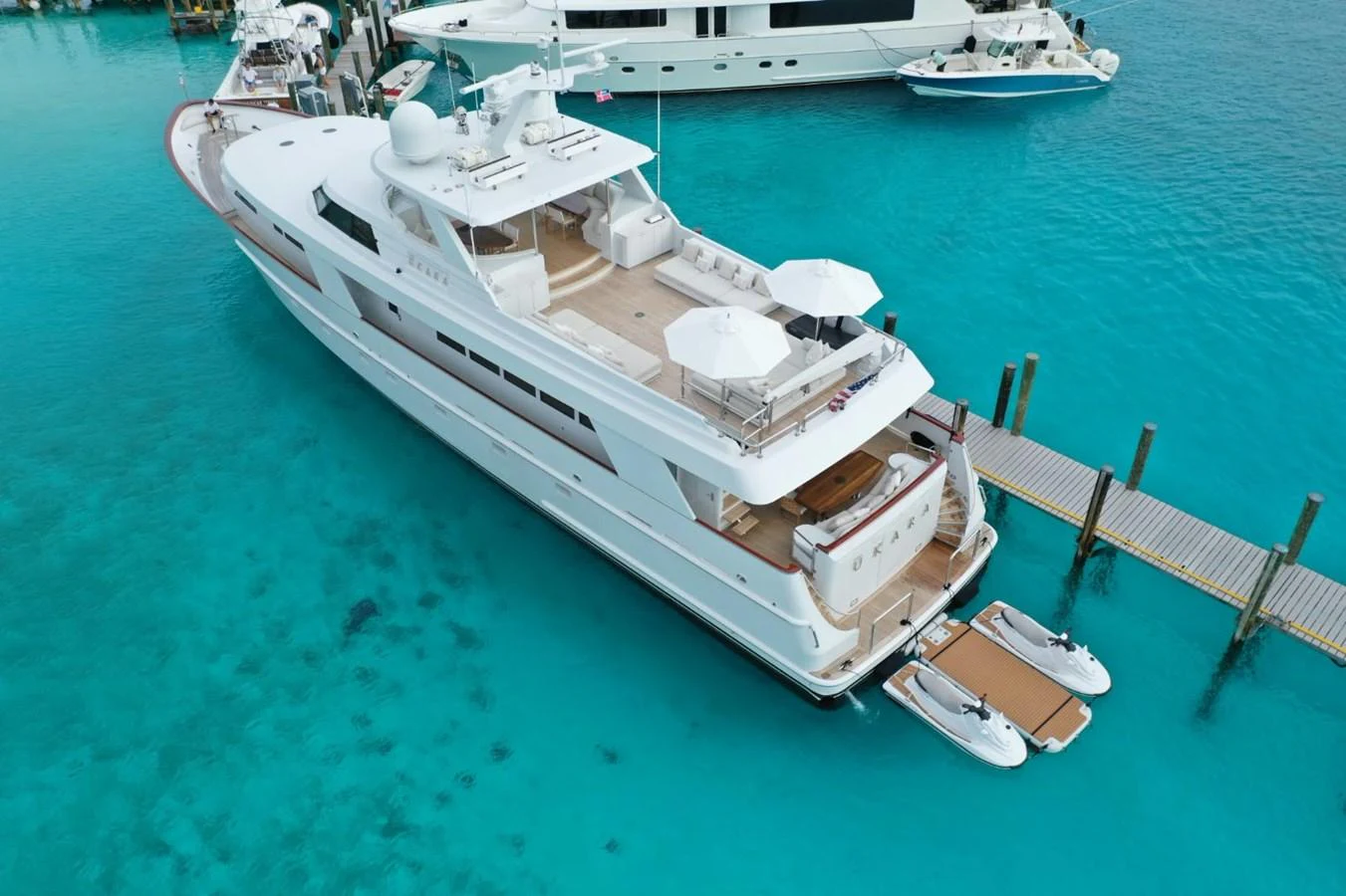 A luxurious yacht is docked in crystal-clear turquoise waters, showcasing its spacious aft deck and tender boats. aboard UKARA Yacht for Sale