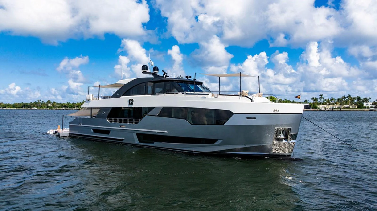 A sleek and modern yacht is anchored on calm waters under a bright blue sky with scattered clouds. aboard M/Y 12 Yacht for Sale