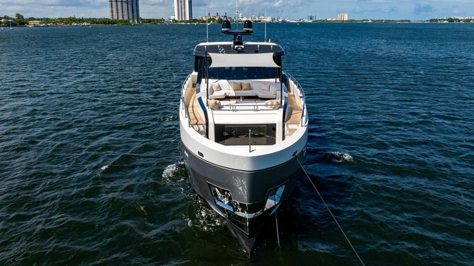 A sleek yacht cruises on calm waters with a cityscape in the background. aboard M/Y 12 Yacht for Sale