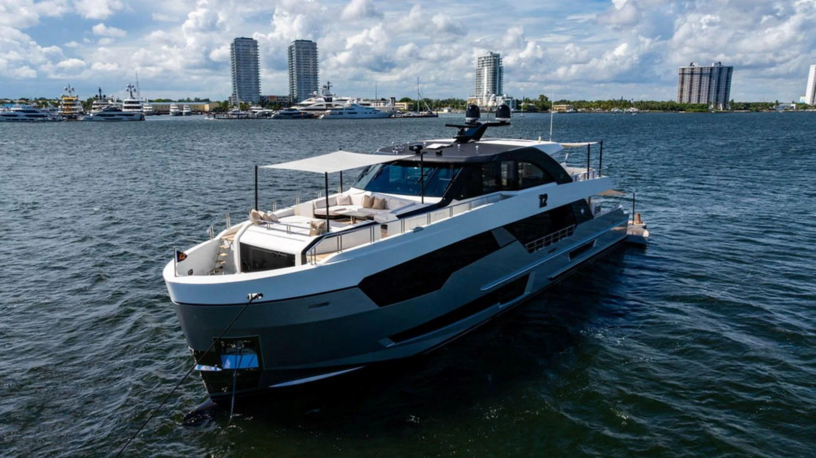 A sleek and modern yacht cruising in a bustling marina with a cityscape in the background. aboard M/Y 12 Yacht for Sale