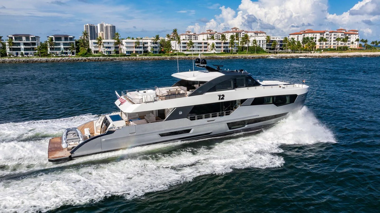 A sleek and modern yacht cruises through the water with a backdrop of coastal residences. aboard M/Y 12 Yacht for Sale