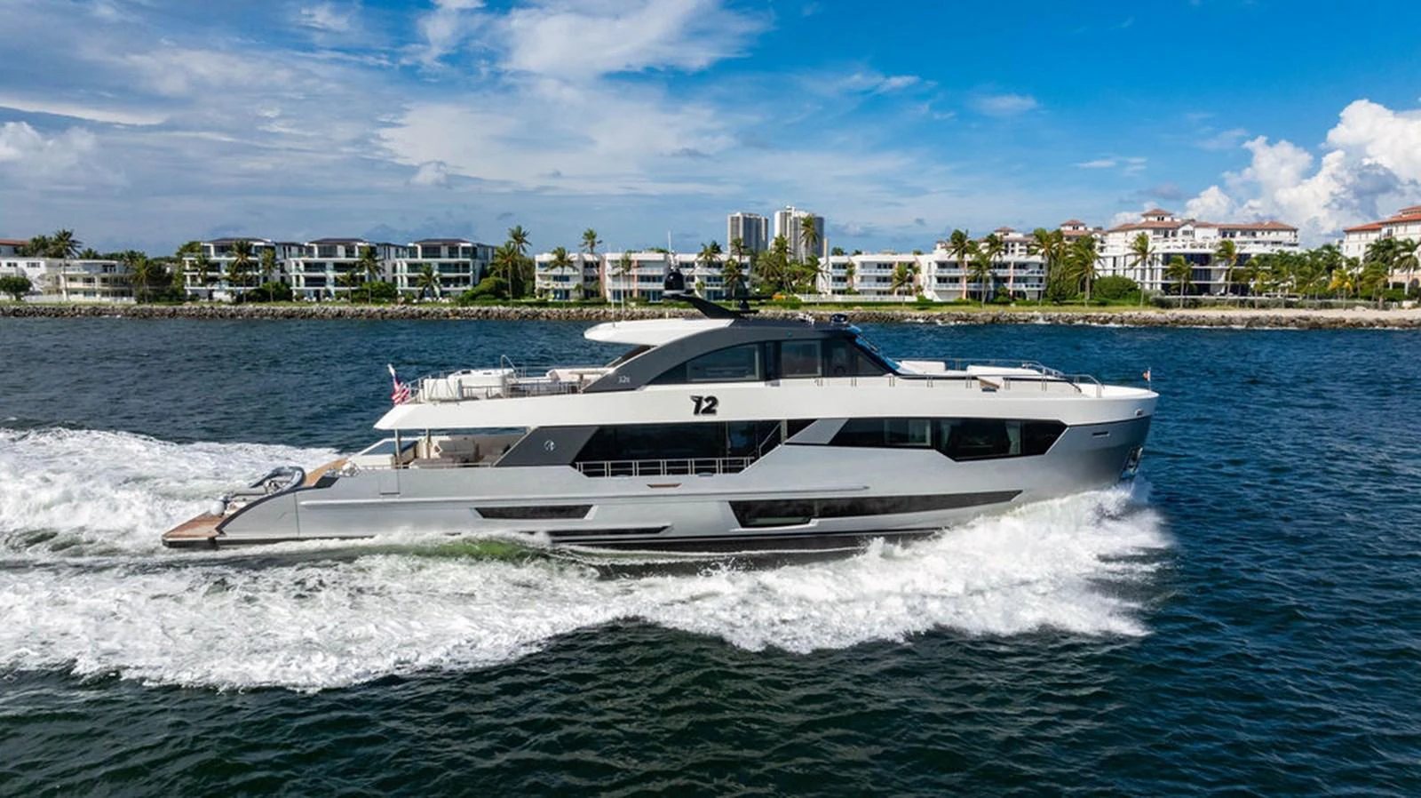 A sleek and modern yacht cruising along the coastline with a backdrop of luxury residences. aboard M/Y 12 Yacht for Sale