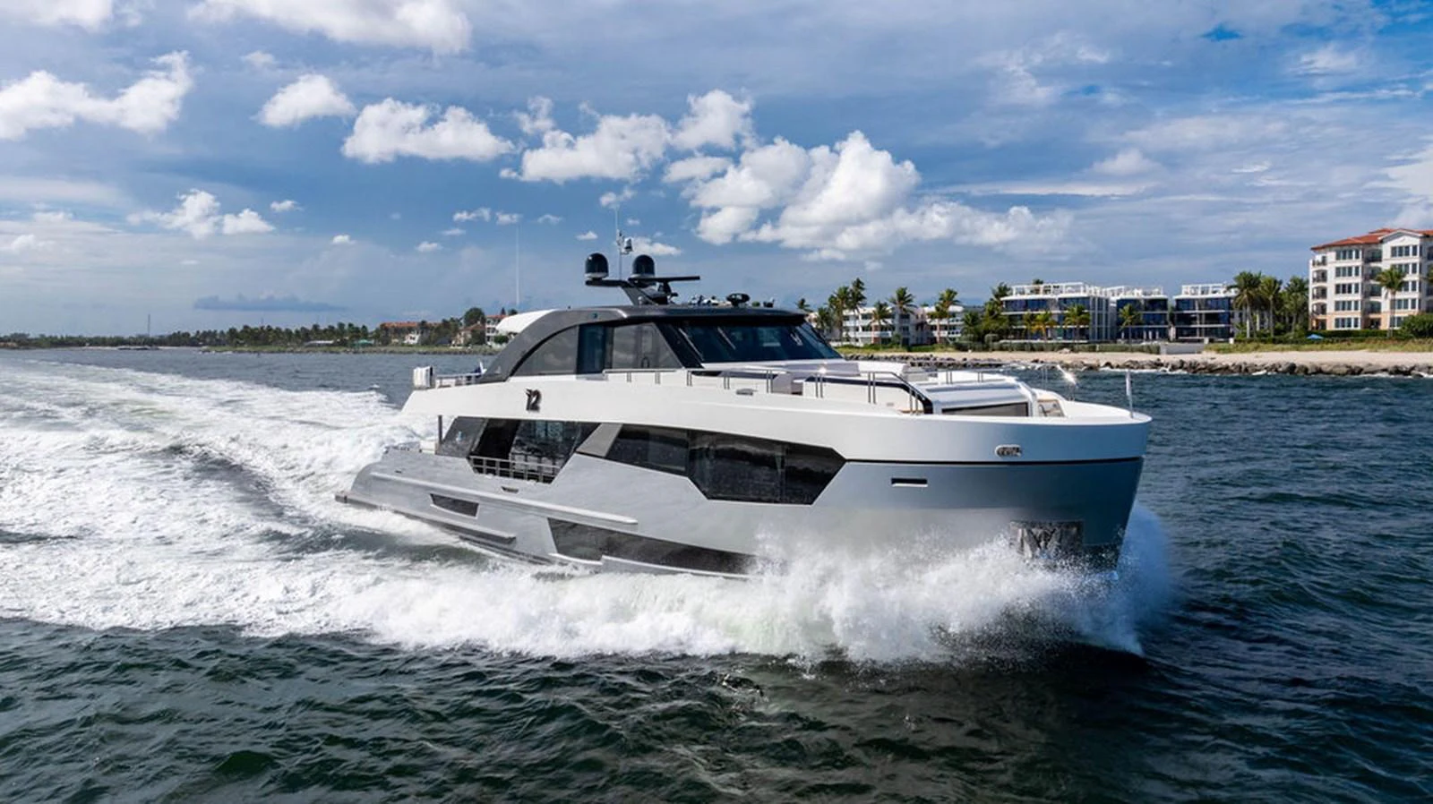 A sleek, modern yacht cruises swiftly through the water near a coastal area. aboard M/Y 12 Yacht for Sale