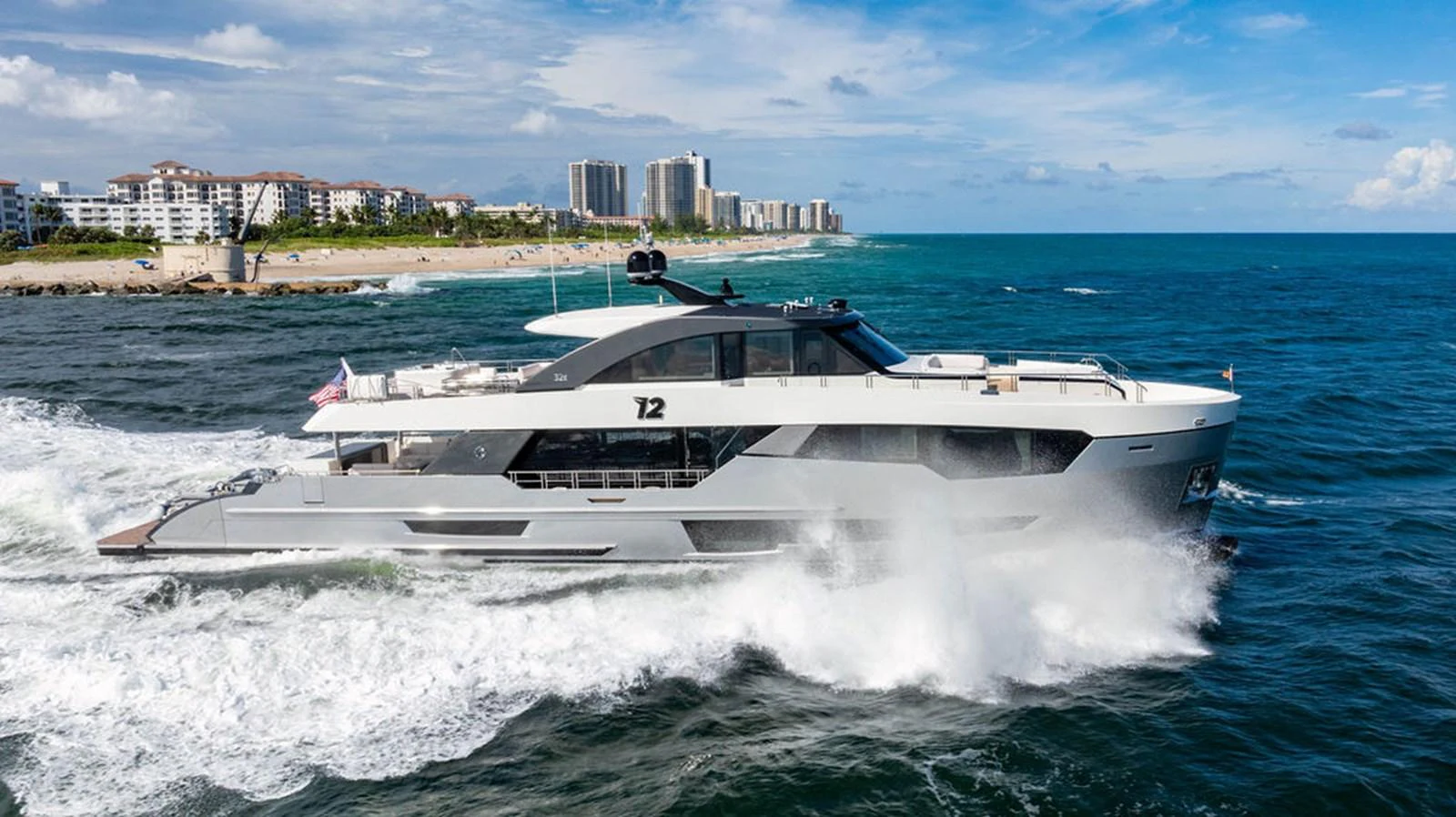 A sleek and modern yacht cruises through the vibrant blue waters near a coastal city. aboard M/Y 12 Yacht for Sale