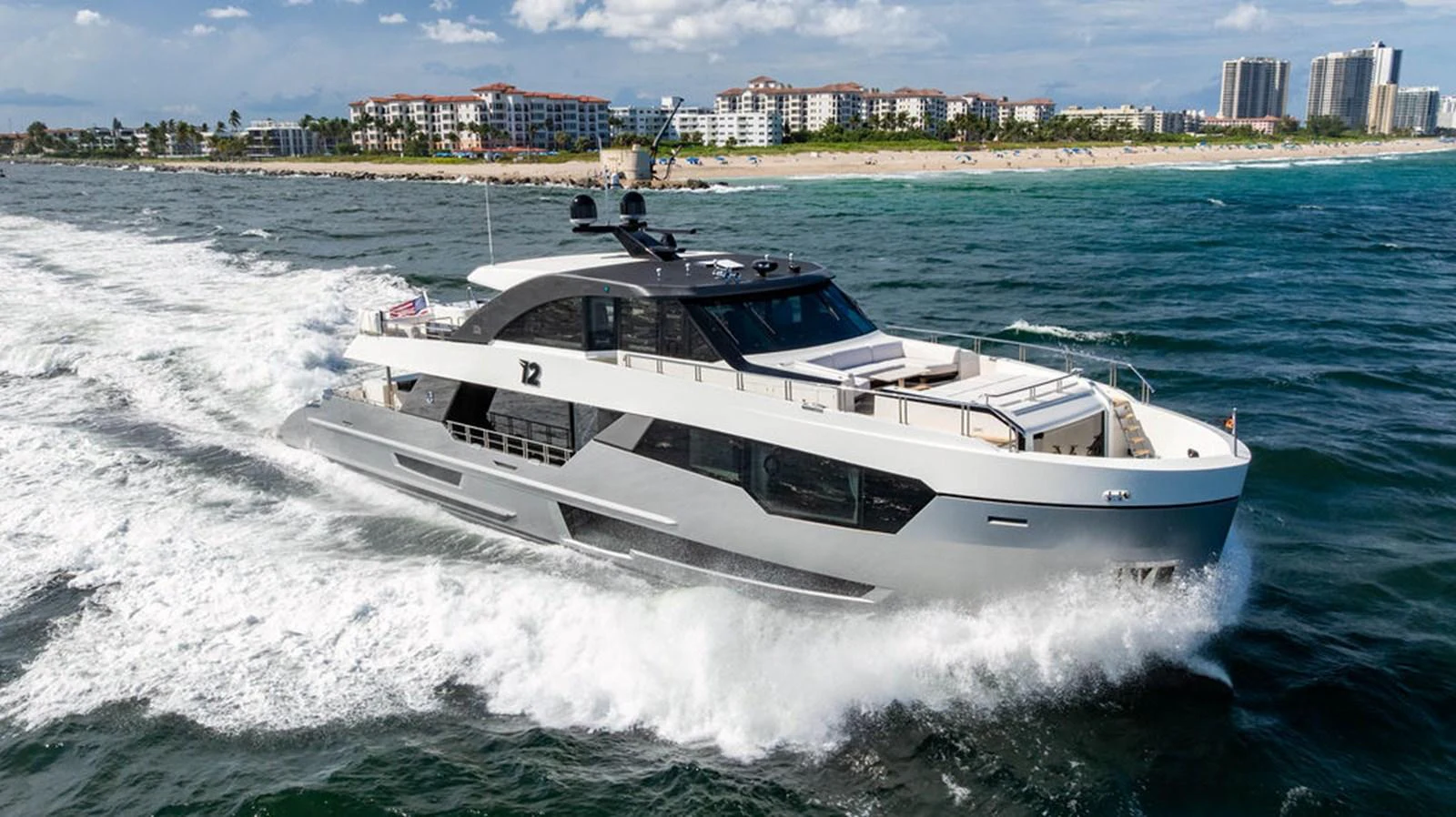 A sleek and modern yacht cruises swiftly through the water near a coastal city. aboard M/Y 12 Yacht for Sale