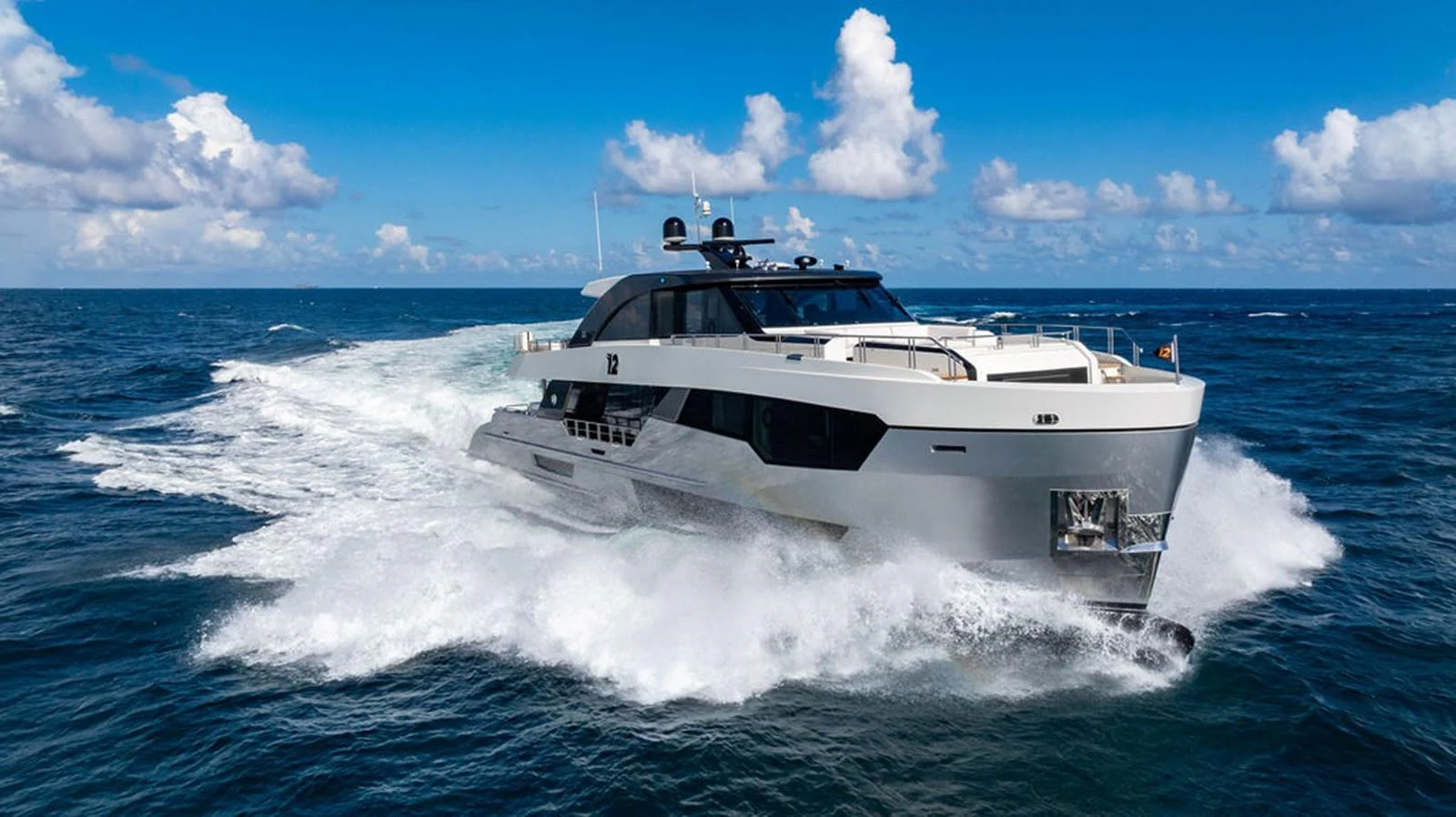 A sleek yacht cuts through the waves under a bright blue sky. aboard M/Y 12 Yacht for Sale