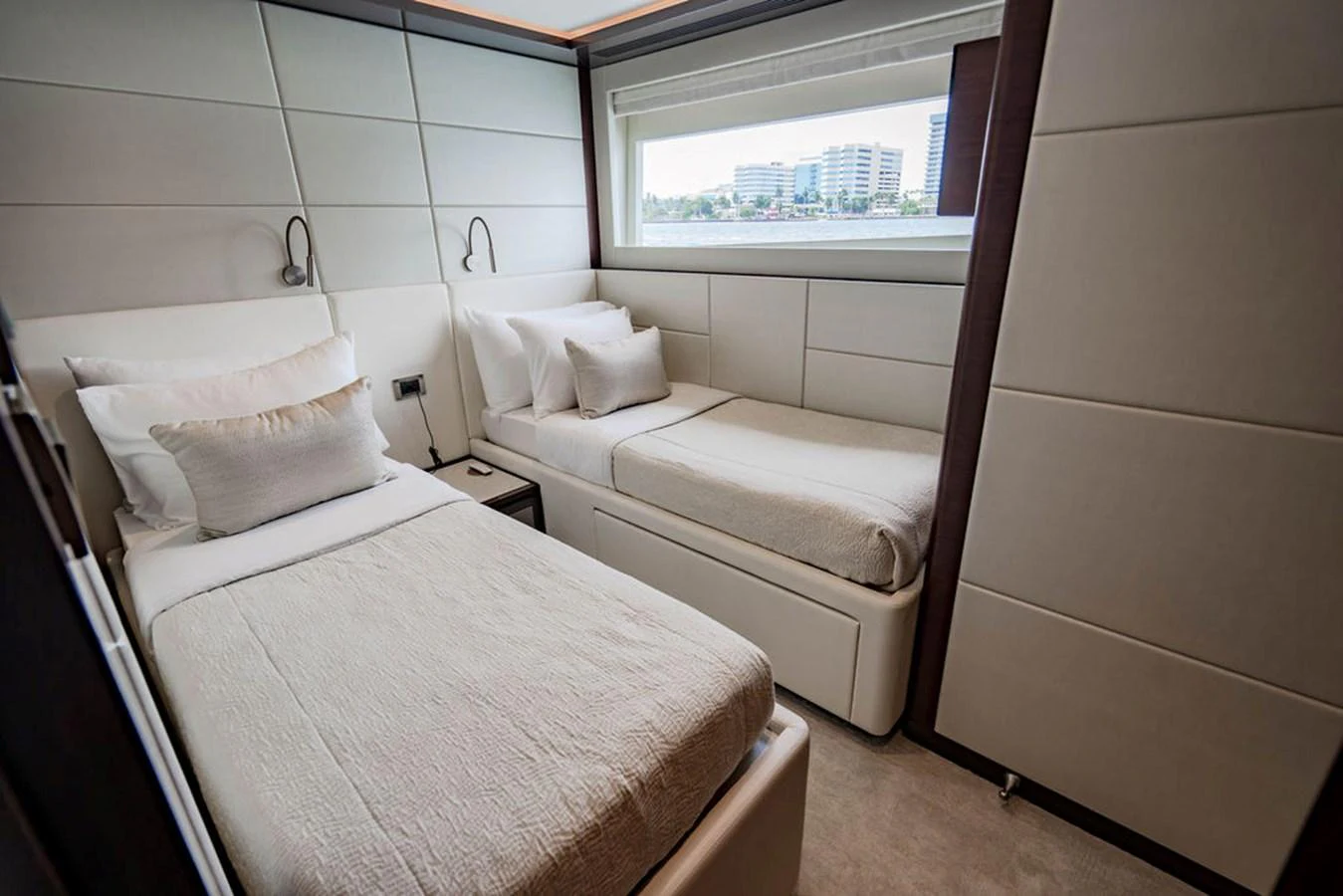 The guest stateroom features twin beds with modern, minimalist decor and a large window offering a view of the water. aboard M/Y 12 Yacht for Sale