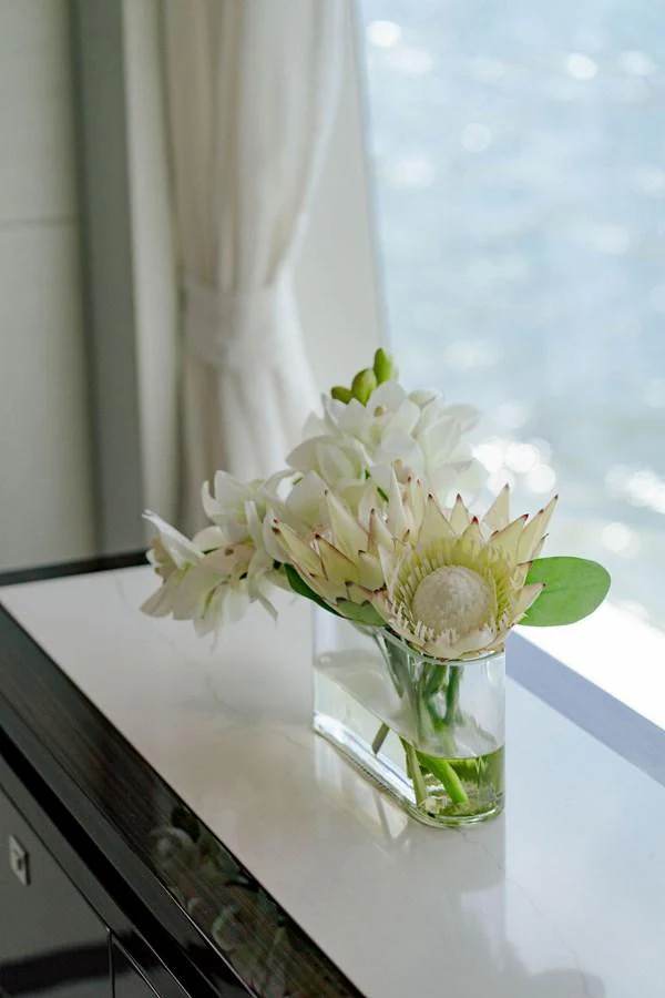 A delicate floral arrangement in a glass vase sits on a polished surface by a window with a serene water view. aboard M/Y 12 Yacht for Sale