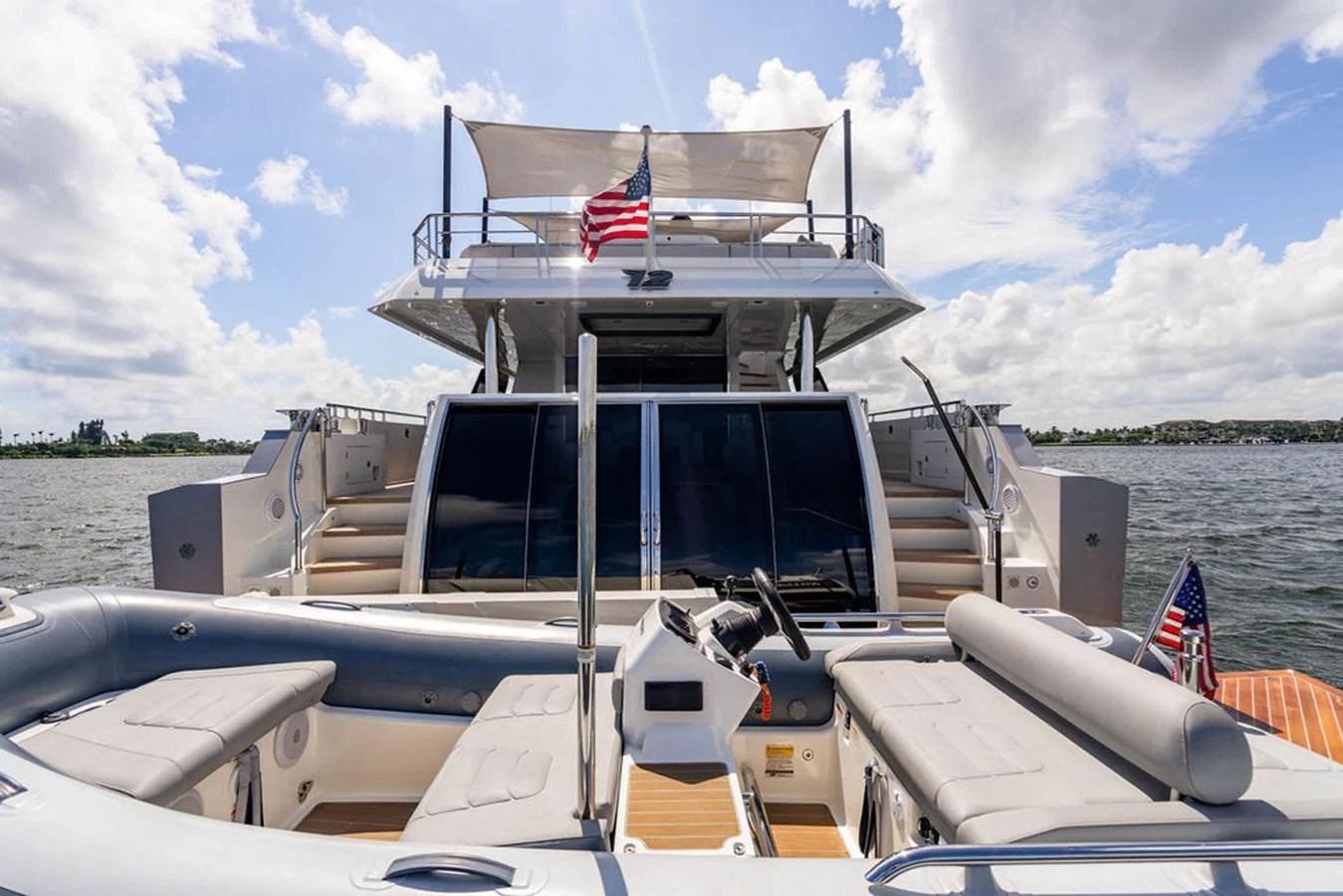 The yacht's aft deck features comfortable seating and a view of the upper deck with an American flag waving in the breeze. aboard M/Y 12 Yacht for Sale