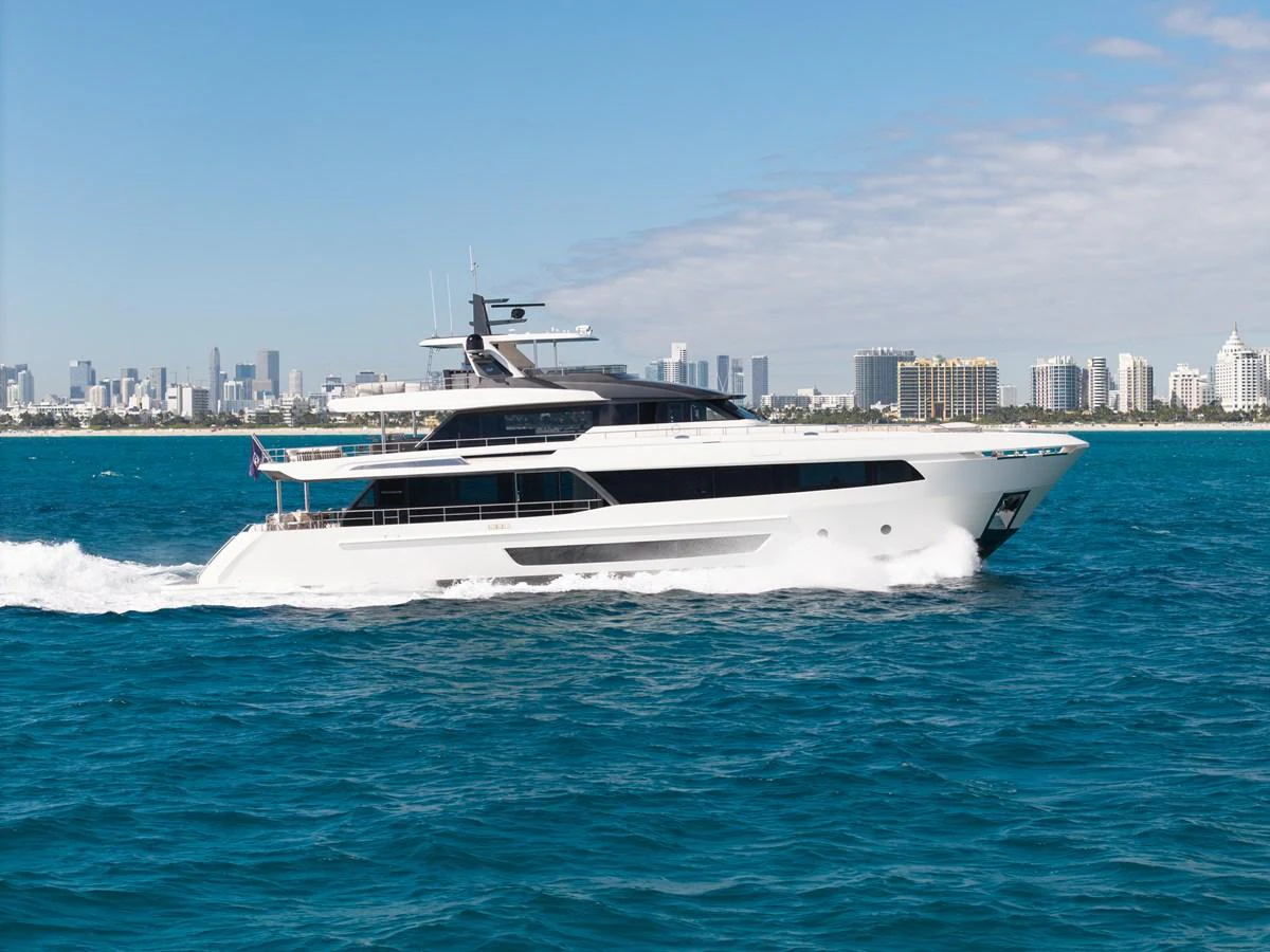 A sleek and modern yacht cruises through the vibrant blue waters with a city skyline in the background. aboard OCEAN ALEXANDER 35P05 Yacht for Sale