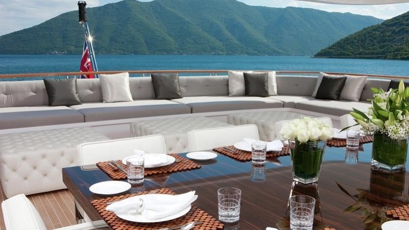 a table with a vase of flowers and a couch with a view of mountains in the background aboard CARPE DIEM Yacht for Charter