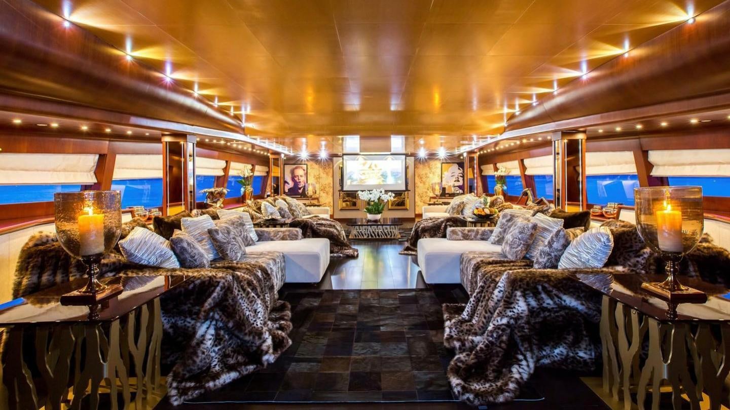 a room with a large couch and a table with chairs and a large window aboard AQUILA Yacht for Charter