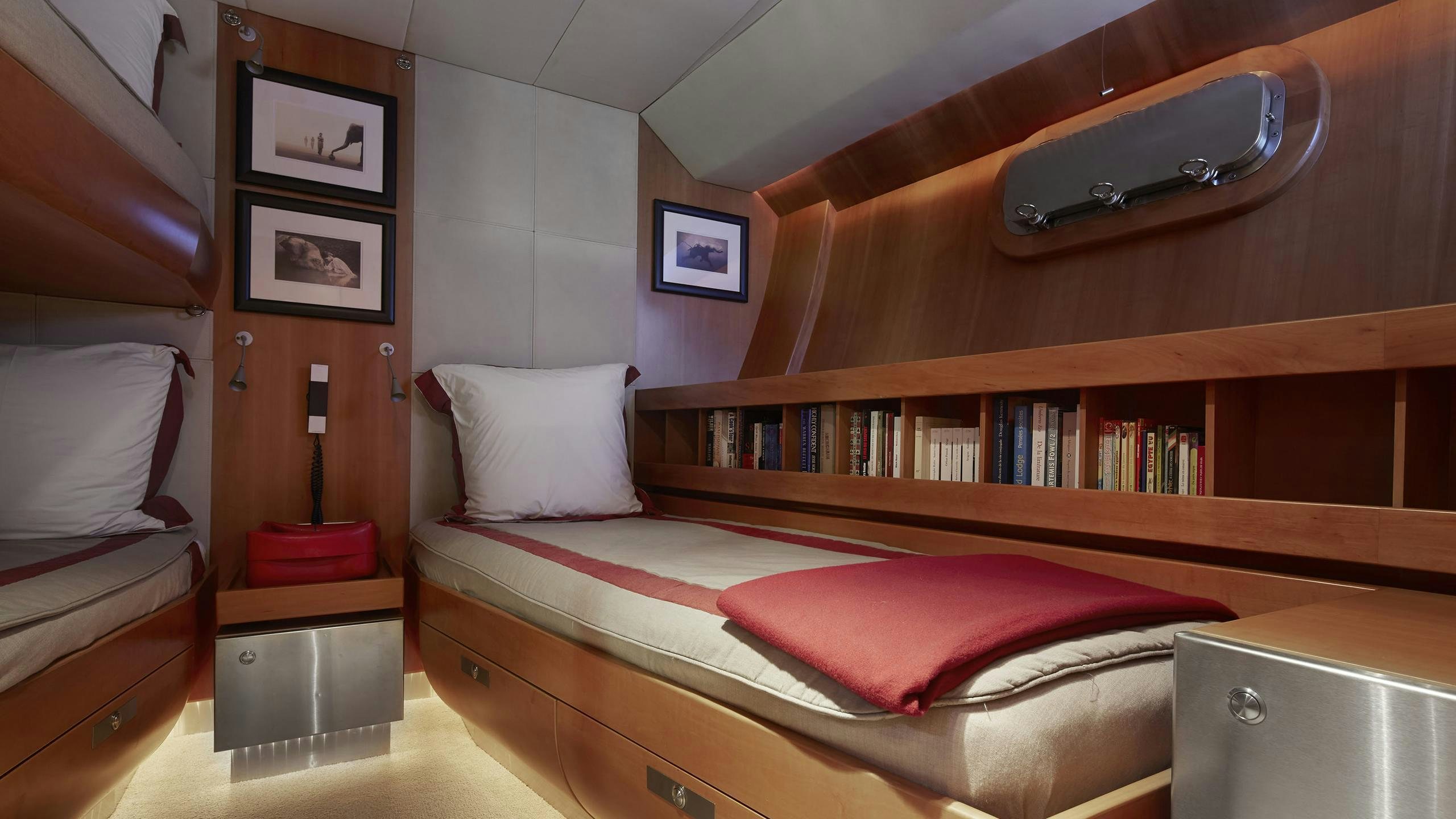 a bed with a red cover and a bookcase aboard SILVERTIP Yacht for Charter