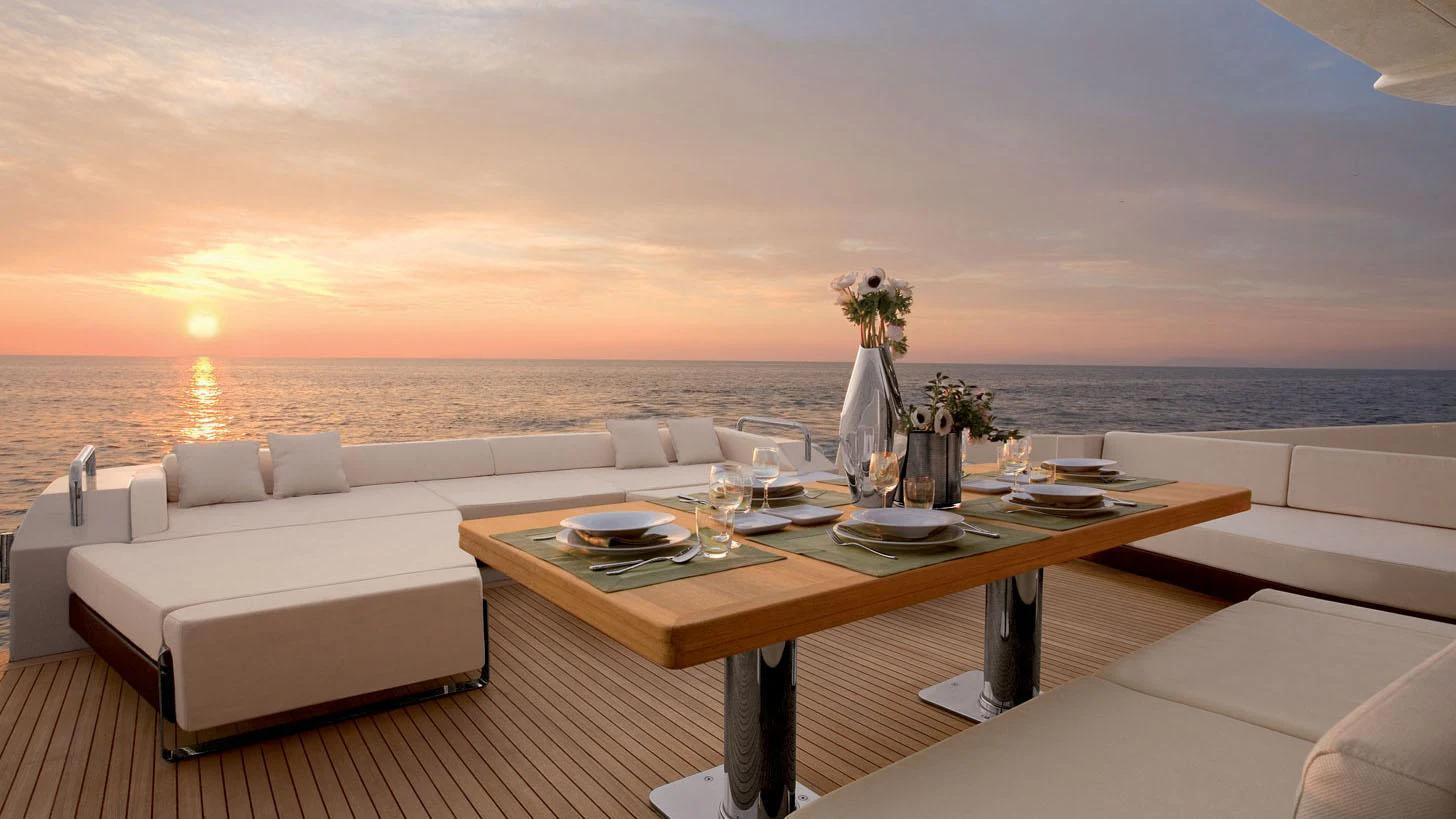 a table with chairs and a couch on a balcony overlooking a sunset aboard DUKE Yacht for Charter