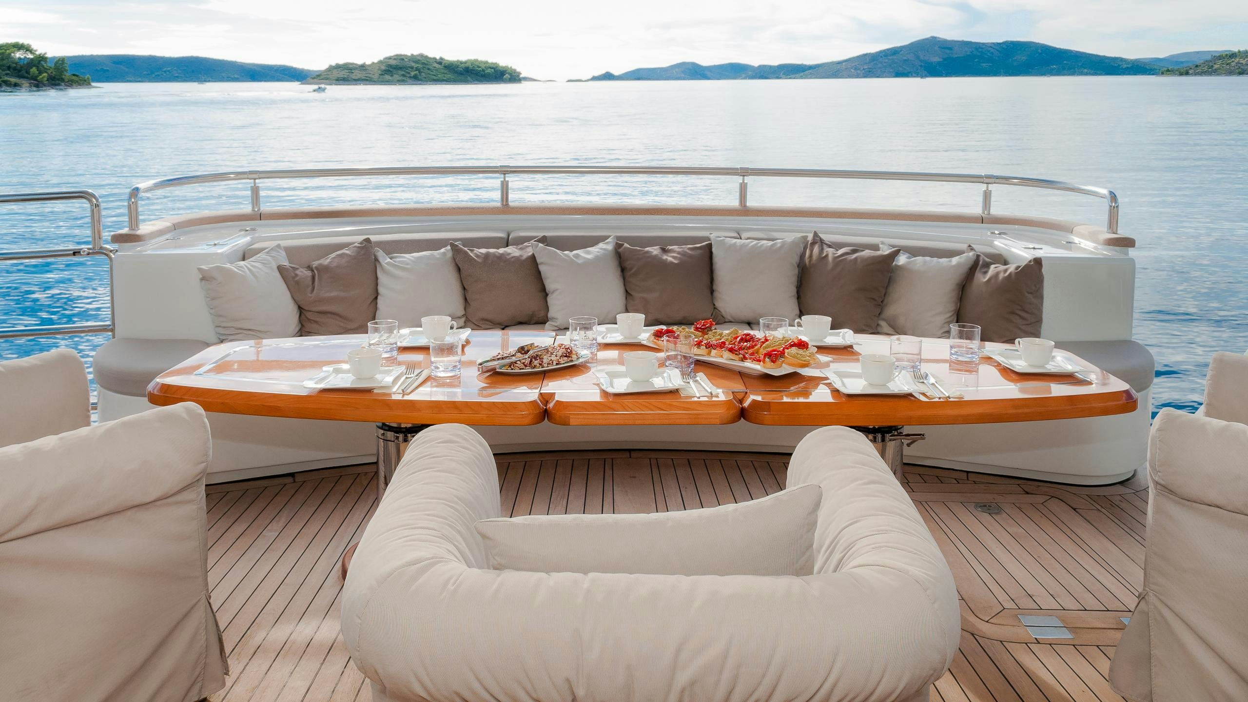 a couch and a table on a deck with a body of water in the background aboard NOVELA Yacht for Charter