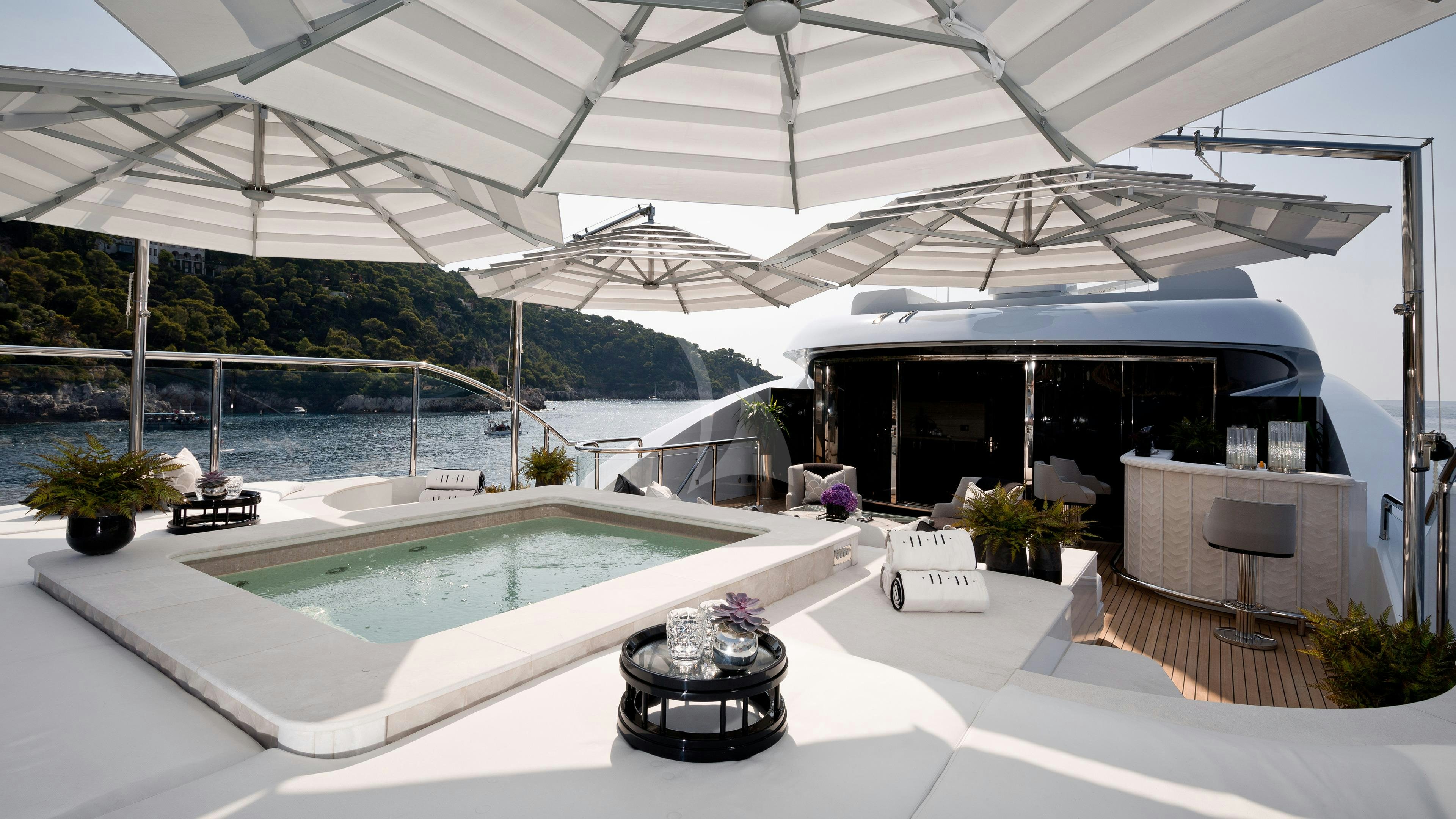 a large white lounge area with a pool and plants and a large glass window with a view of aboard SOUNDWAVE Yacht for Charter