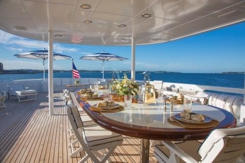 a table with plates and glasses on it on a deck with a view of the ocean and blue aboard CHANTAL MA VIE Yacht for Charter