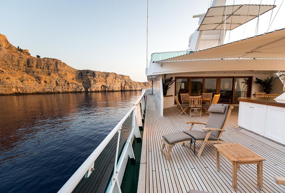 a deck with chairs and tables on it by a body of water aboard ESMERALDA Yacht for Charter