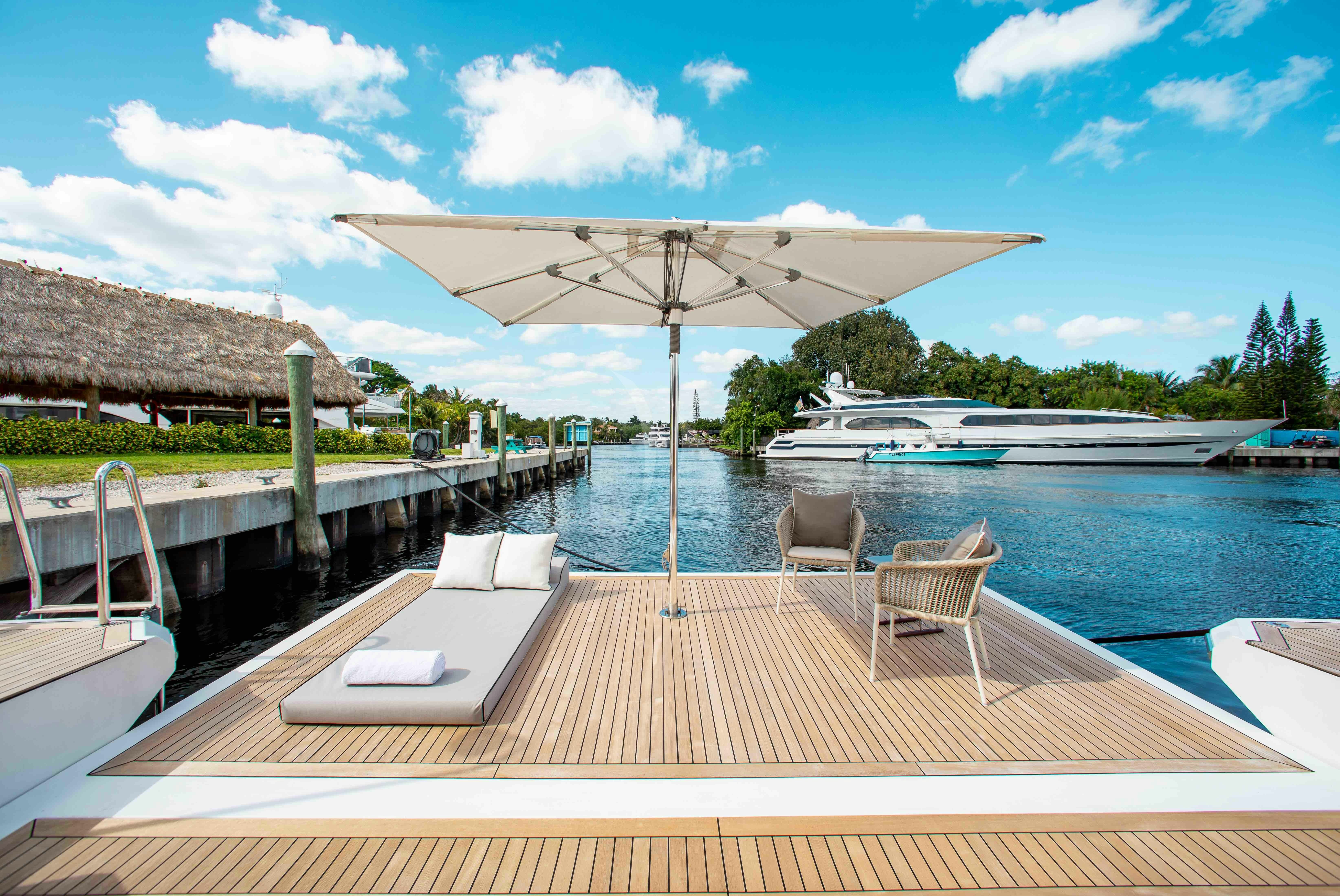 a deck with chairs and a table on it by a body of water aboard EMINA Yacht for Charter