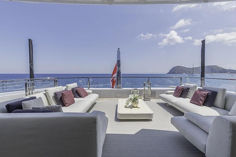 a large white lounge chair with a white table and white couches on a beach with a flag aboard LEL Yacht for Charter