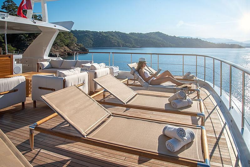 a person lying on a lounge chair on a deck overlooking a body of water aboard SUNRISE Yacht for Charter