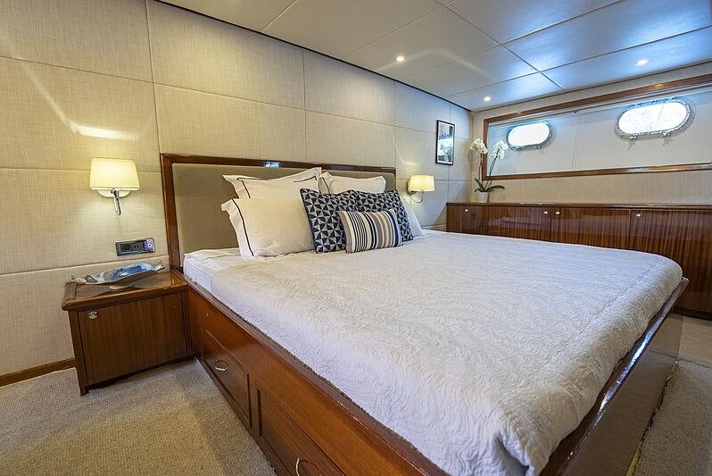 a bed with a white comforter and pillows in a room with a wood wall and a window aboard ALHAMBRA Yacht for Sale