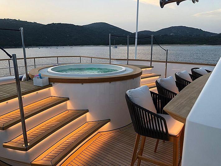 a table with chairs and a pool on a deck overlooking a body of water aboard ROBBIE BOBBY Yacht for Charter