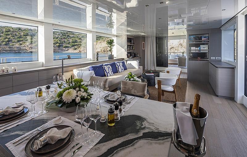 a large dining table with a white couch and white chairs aboard DINAIA Yacht for Charter