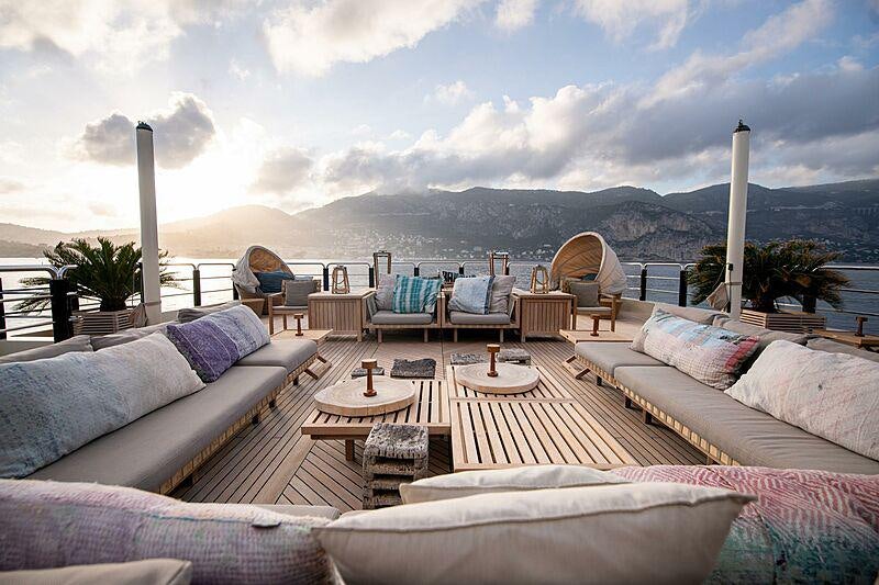 a patio with a table chairs and a large white building with a view of mountains and water aboard ARBEMA Yacht for Charter