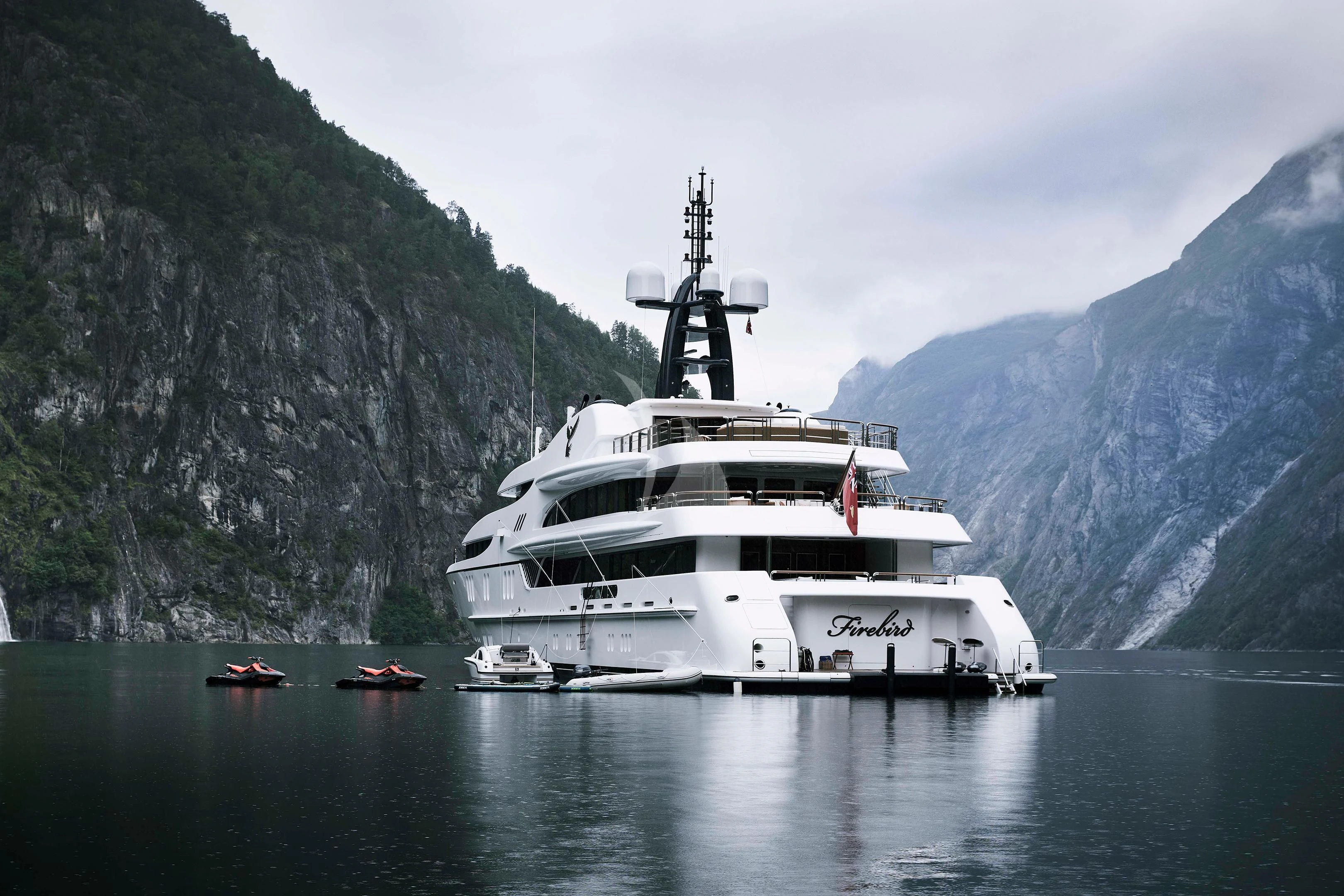 a white boat in the water with Geirangerfjord in the background aboard FIREBIRD Yacht for Charter