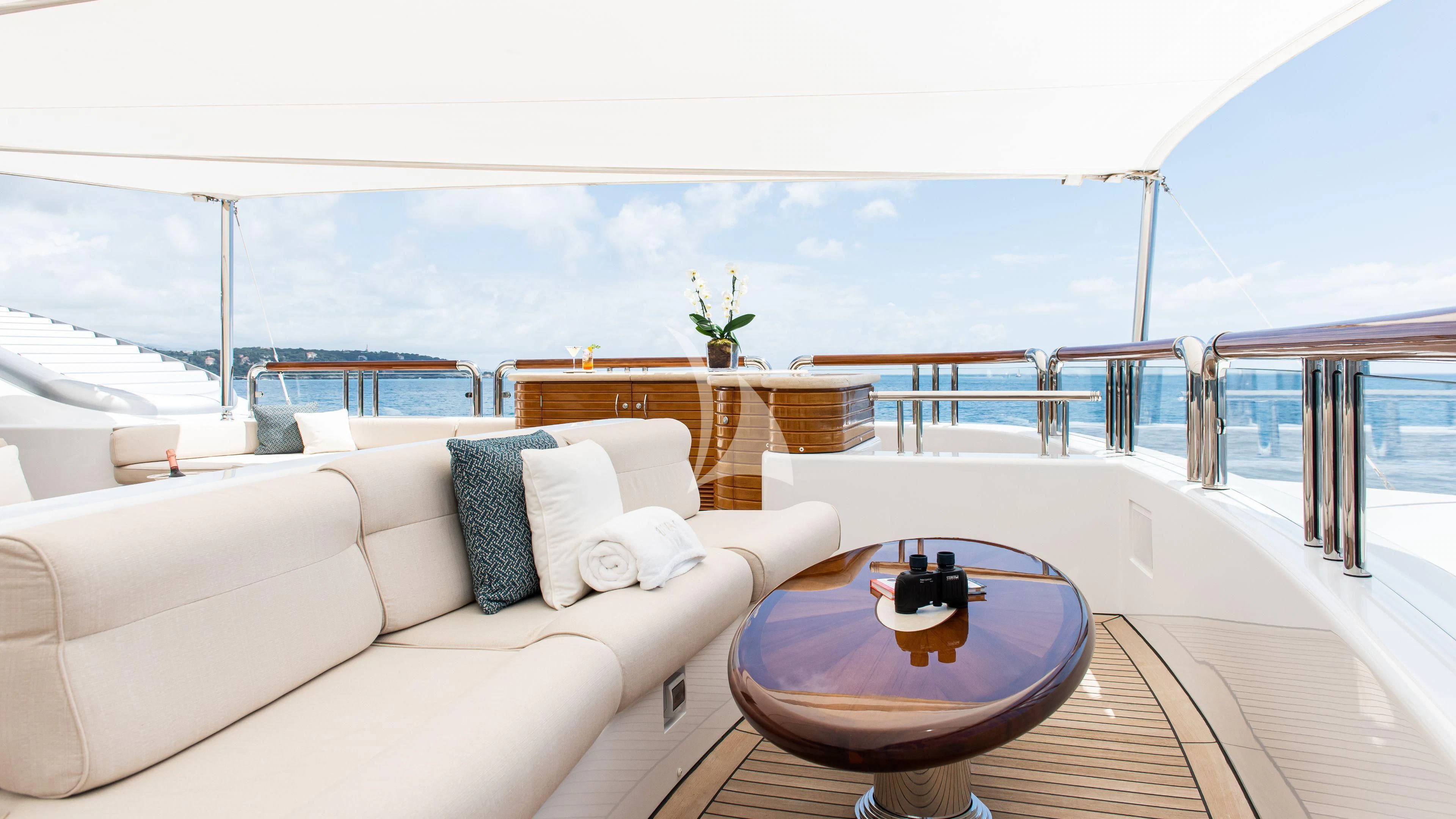 a large white sofa and a table on a balcony overlooking a body of water aboard FIREBIRD Yacht for Charter