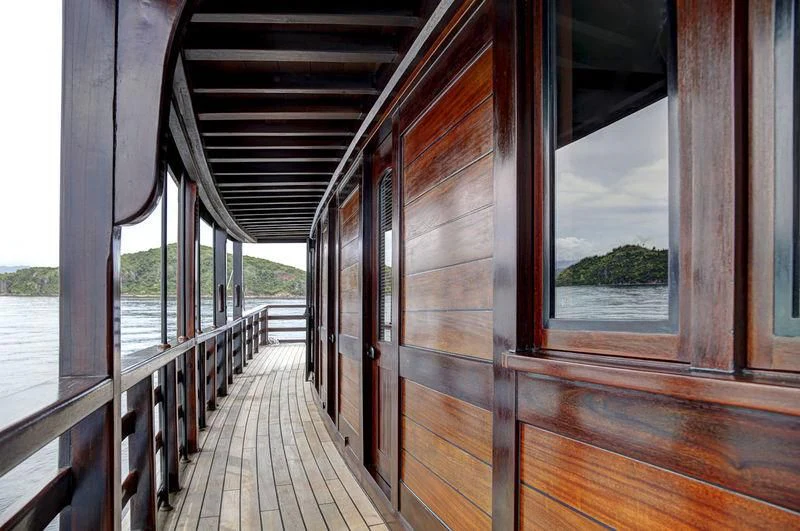 a wood deck with a wood railing and a railing with a building in the background aboard DUNIA BARU Yacht for Charter