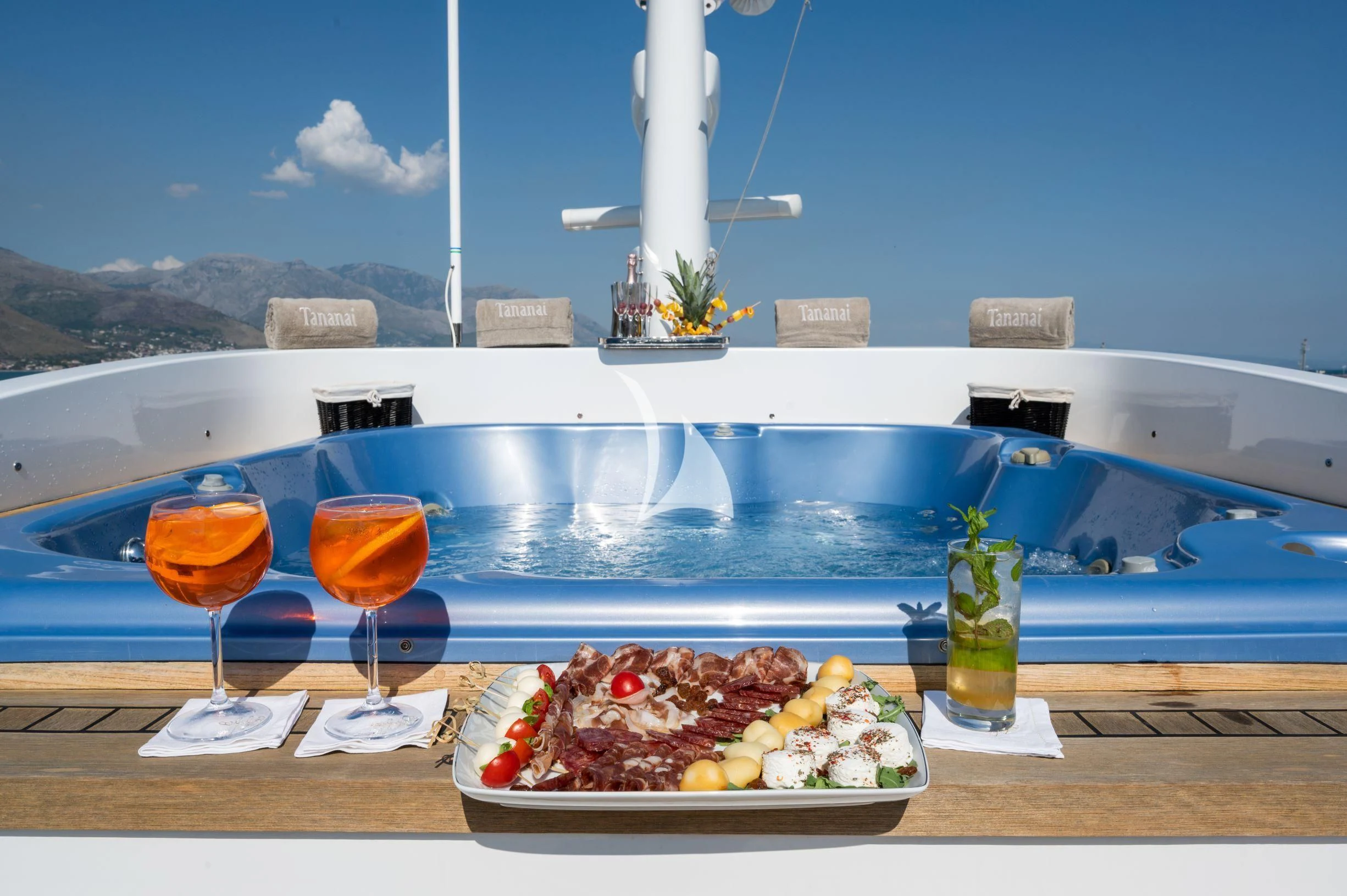 a plate of food and glasses of wine on a table by a pool aboard TANANAI Yacht for Sale