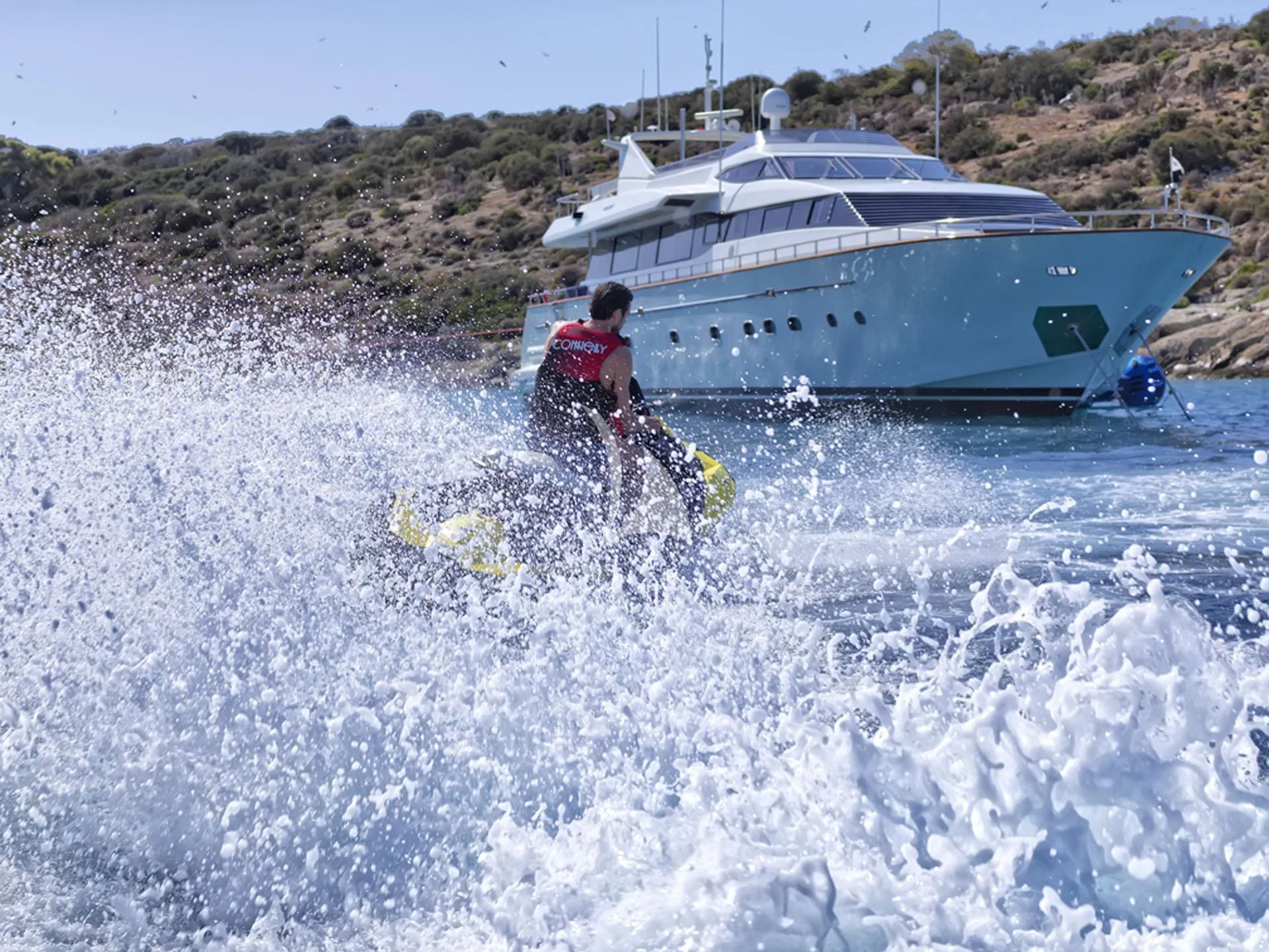a person riding a surfboard in the water next to a boat aboard MANTRA Yacht for Sale