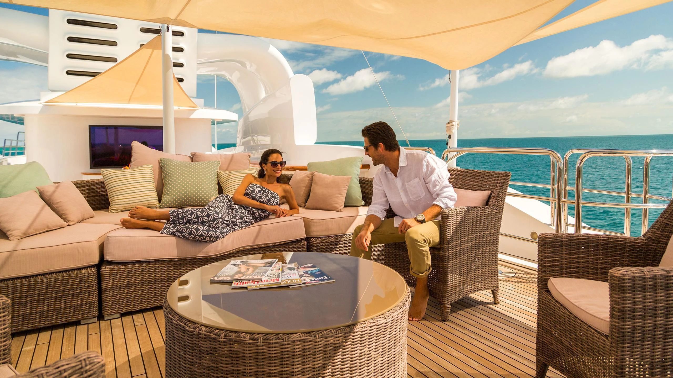 a man and woman sitting on a couch on a deck with a large white tent behind them aboard SORRENTO Yacht for Sale