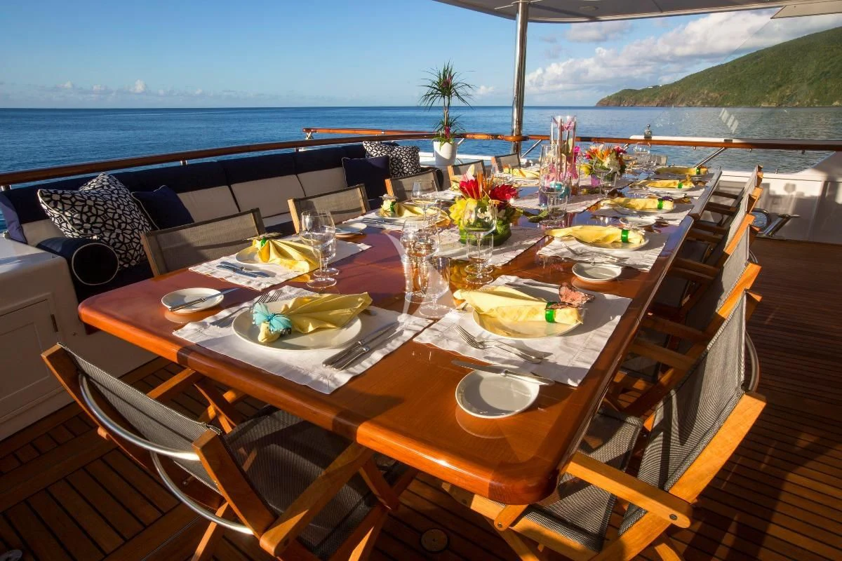 a table set with plates and glasses on a patio overlooking the ocean aboard TELEOST Yacht for Sale