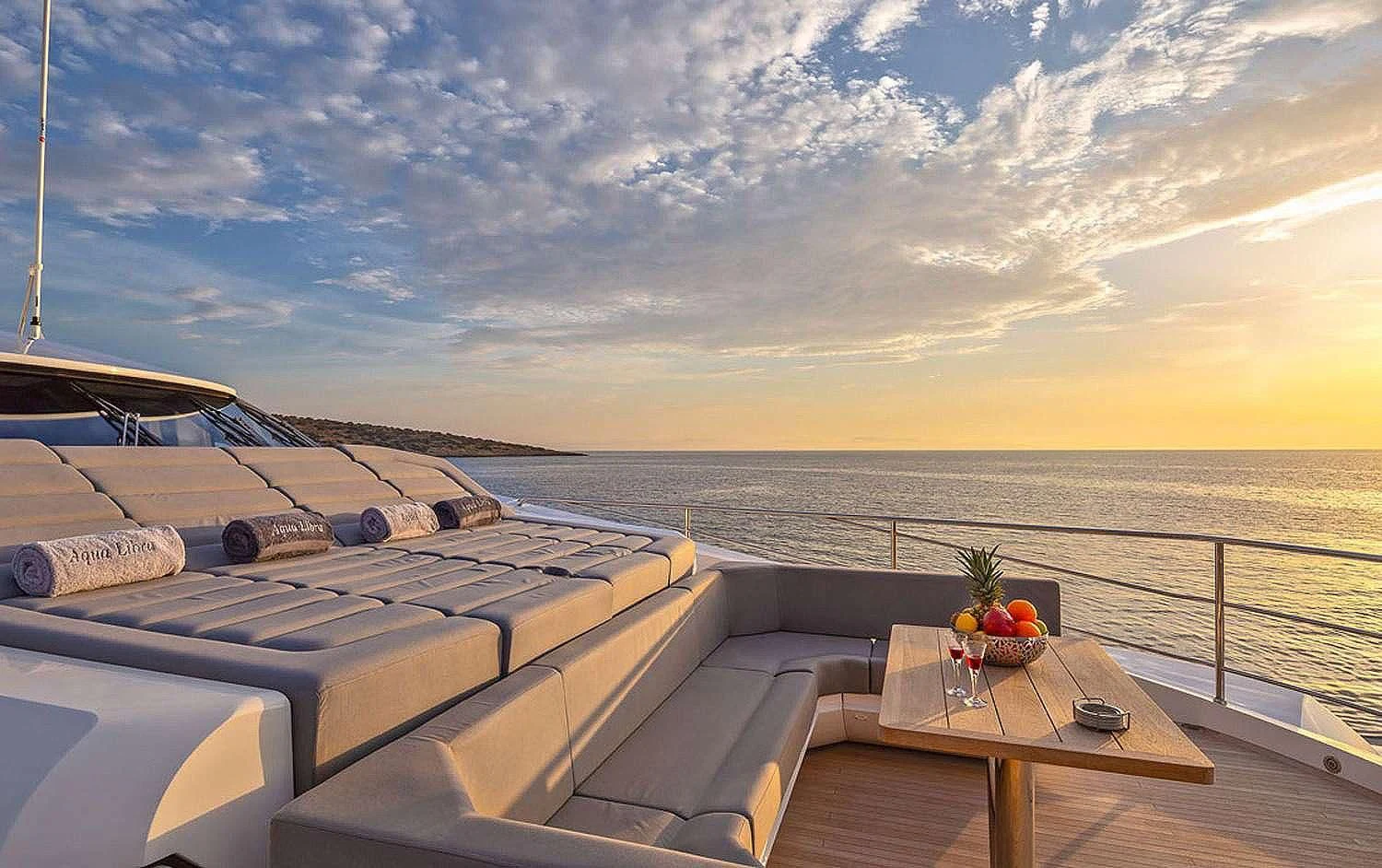 a deck with a view of the ocean and the sun setting aboard AQUA LIBRA Yacht for Charter