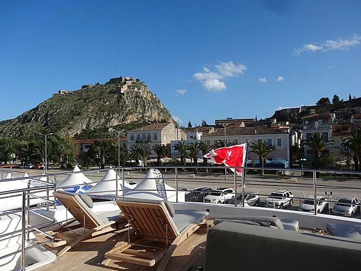 a deck with a flag and a mountain in the background aboard AQUA LIBRA Yacht for Charter